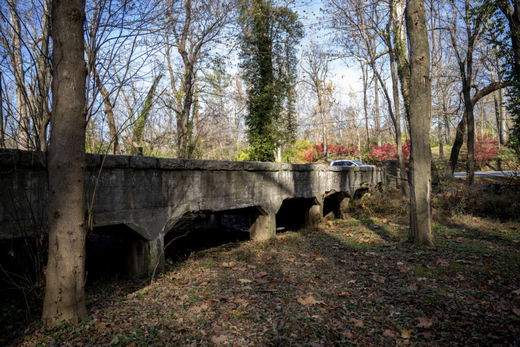 A stone bridge in Kentucky. There are fall leaves on the ground. The sky is blue.