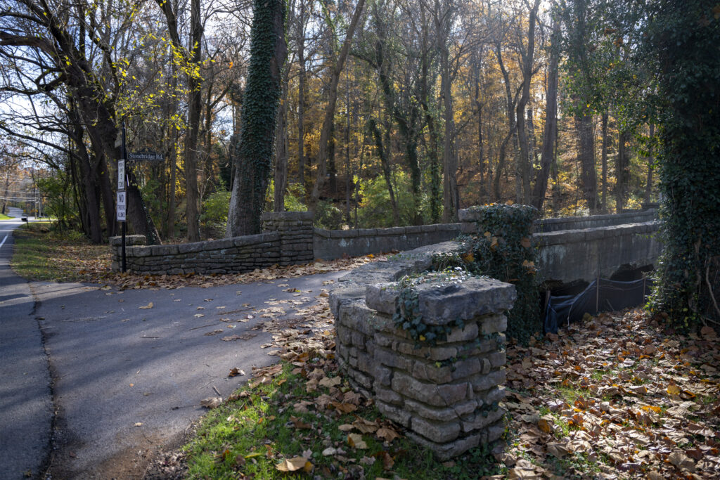 Concrete approach of a stone bridge. It is fall, and many trees have lost leaves.